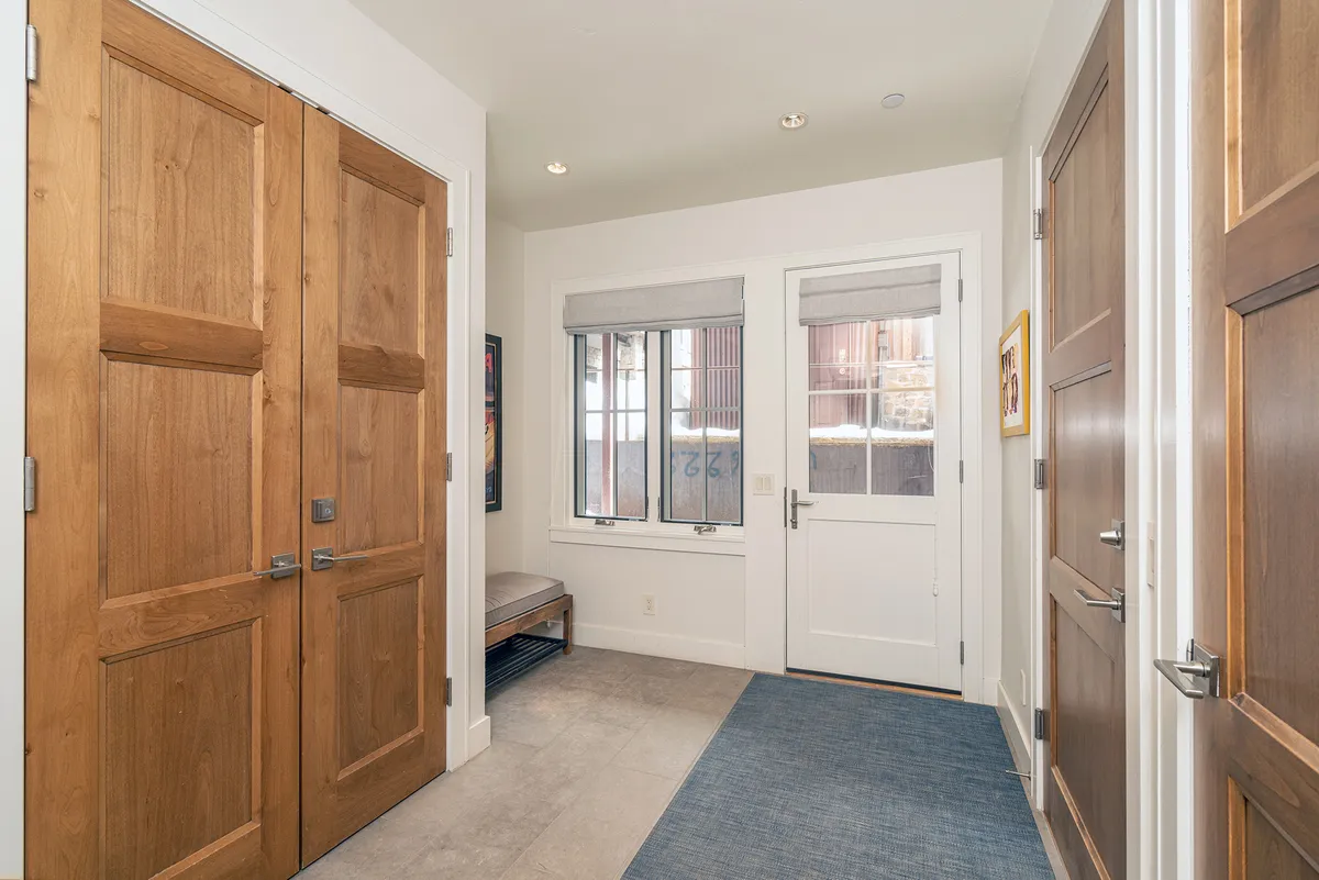 A welcoming entryway featuring double wooden doors, a window allowing in natural light, bench seating for convenience, and tasteful decorative artwork. The scene suggests a well-organized and inviting transition space between the outdoors and the interior living areas.