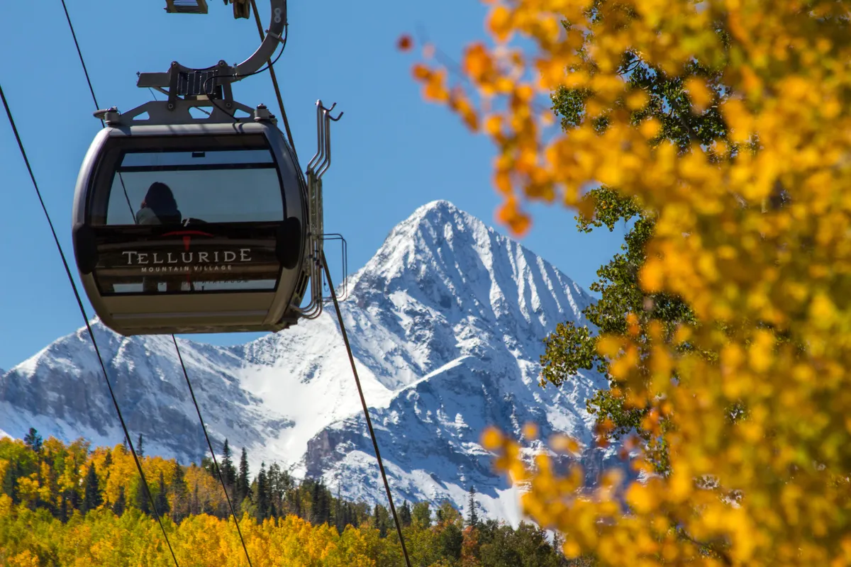 This image captures the gondola ascending against a backdrop of snow-capped mountains and vibrant autumn foliage, highlighting a quintessential Telluride experience right at the doorstep. The gondola is a central feature, illustrating the proximity and easy access to both ski slopes and scenic hikes.