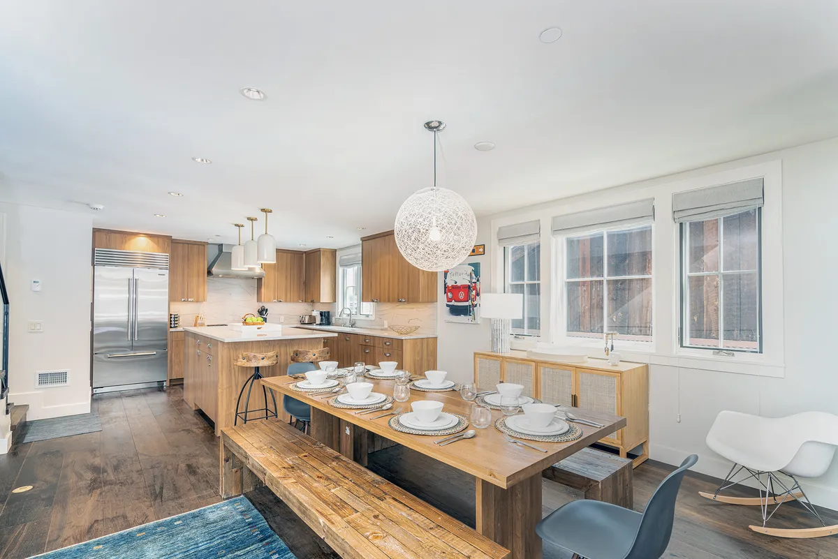 The hero image showcases a spacious, warmly lit dining area centered around a large wooden table—perfect for gatherings. Overhead, a striking modern pendant light enhances the stylish ambiance, while the kitchen’s sleek stainless steel appliances promise both functionality and flair. The scene evokes a sense of togetherness, ideal for sharing meals and memorable moments with loved ones.