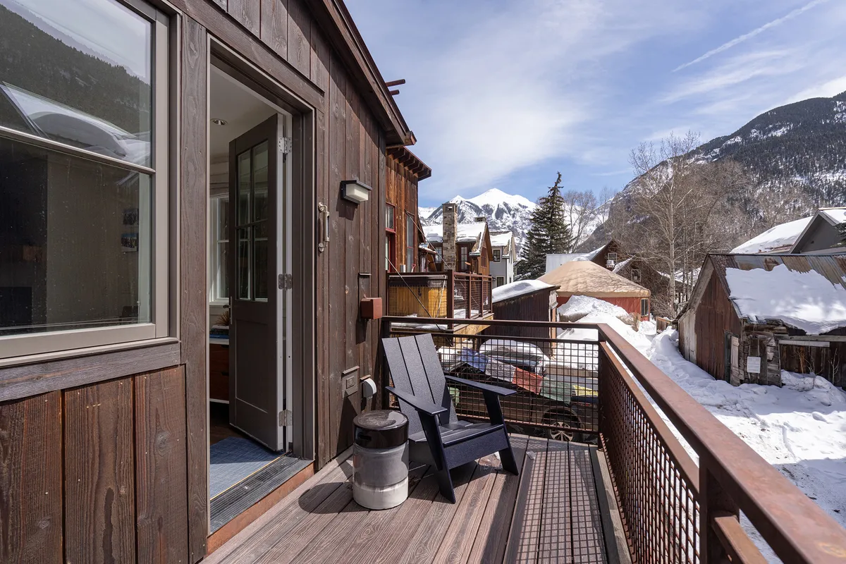 A spacious balcony with black chairs and a stunning mountain view, accessed through doors leading from the living area. The scene suggests a peaceful spot for morning coffee or sunset cocktails, emphasizing the indoor-outdoor connection and scenic backdrop.