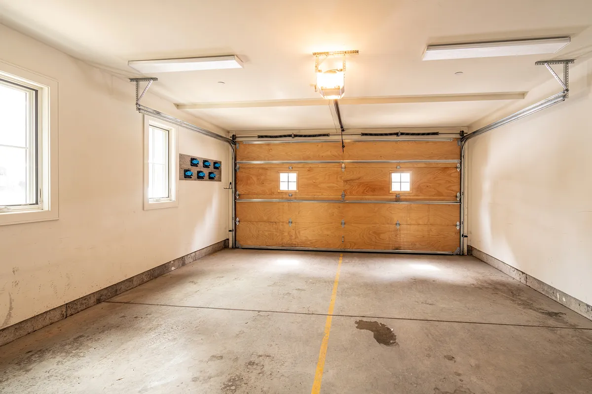 A practical garage interior with a clear view of the garage door, windows for daylight, and functional lighting. The organized space suggests ample room for storing vehicles and outdoor gear, reinforcing convenience and readiness for adventure.