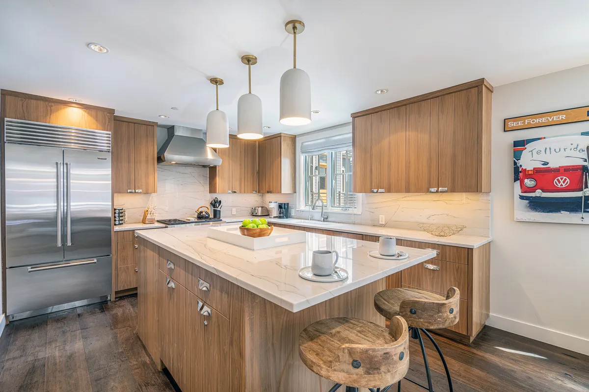 A close-up of the gourmet kitchen featuring a marble island countertop, high-end stainless steel appliances, pendant lighting, and sleek wooden cabinetry. The area is designed for both culinary creativity and social interaction, inviting guests to gather around while meals are prepared.