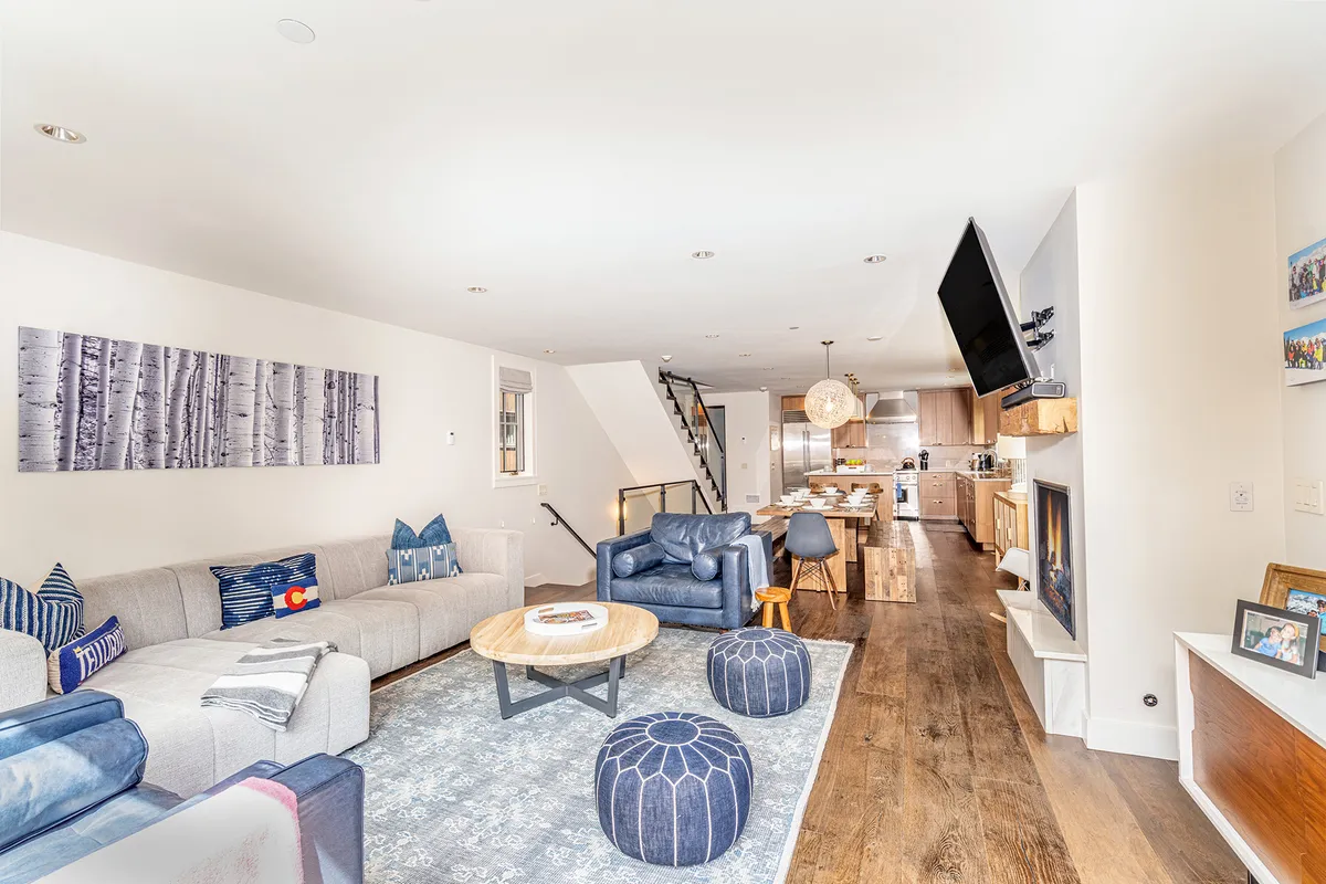 A spacious and inviting living area featuring a comfortable sofa, a modern coffee table, a striking piece of artwork on the wall, a cozy fireplace, and an open kitchen area in the background. The scene is filled with natural light and radiates a warm, welcoming atmosphere, perfect for family relaxation and gatherings.