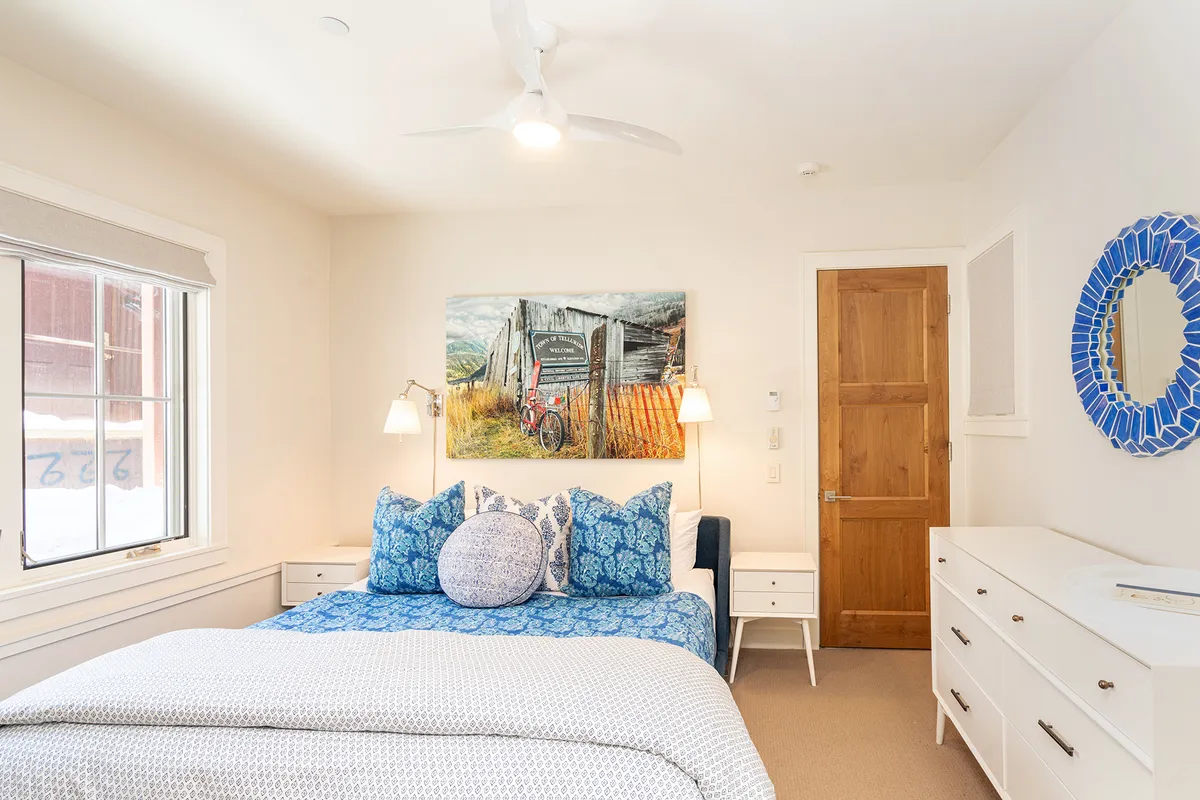 A serene bedroom with a bed dressed in blue patterned bedding, rustic bicycle artwork, and a mirrored decor piece. The room exudes tranquility and privacy—ideal for guests seeking a quiet retreat on the ground floor.